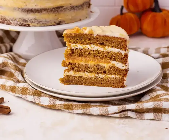 A slice of moist pumpkin cake topped with cream cheese frosting and cinnamon dust