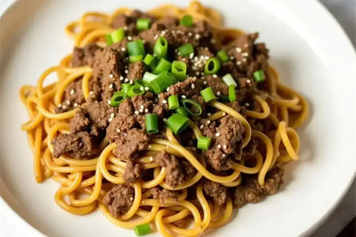 A steaming bowl of Mongolian Ground Beef Noodles garnished with sesame seeds and green onions.